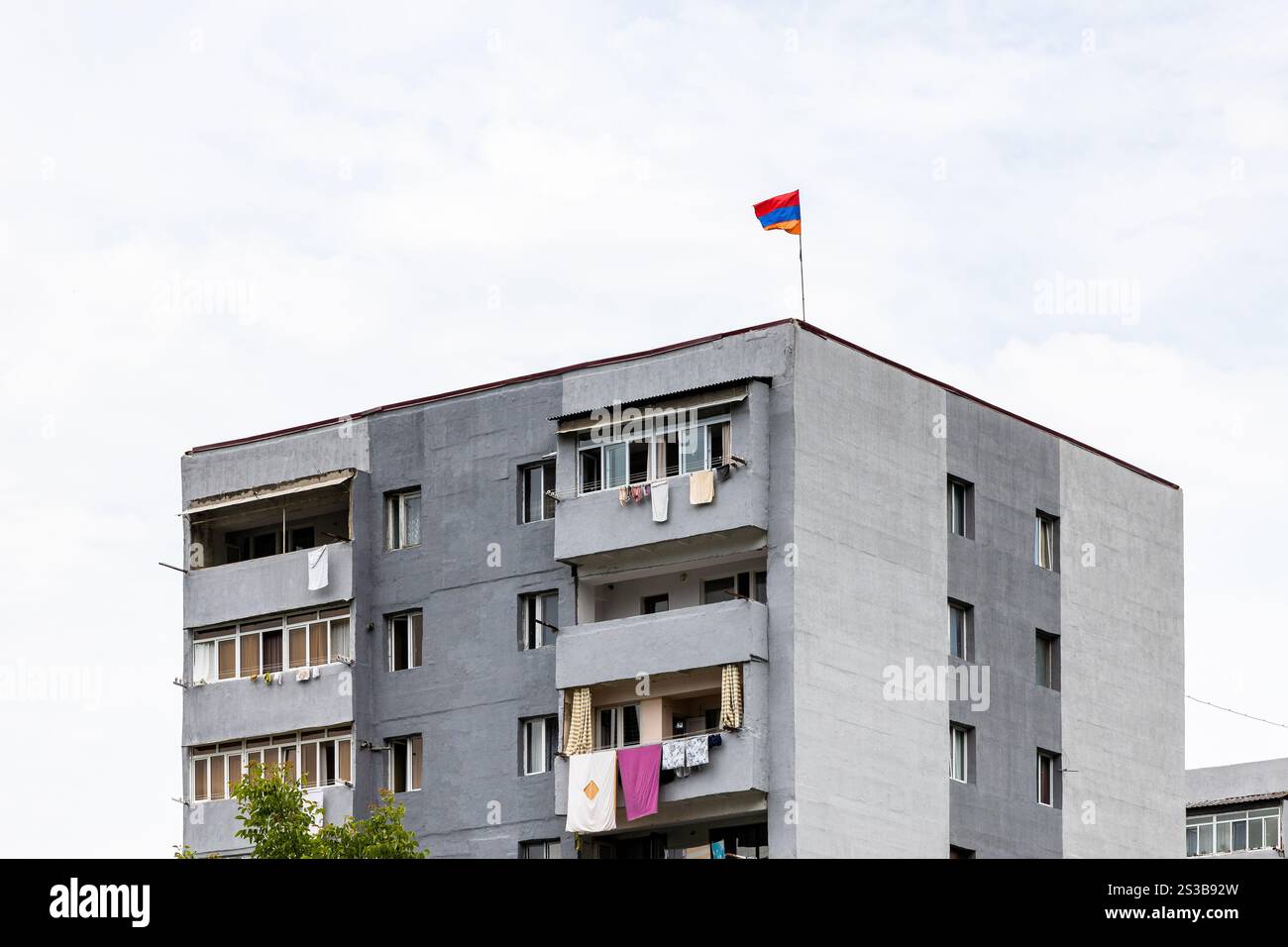 Bandiera armena in cima al moderno edificio di appartamenti nella città di Dilijan, in Armenia, nelle nuvolose giornate estive Foto Stock
