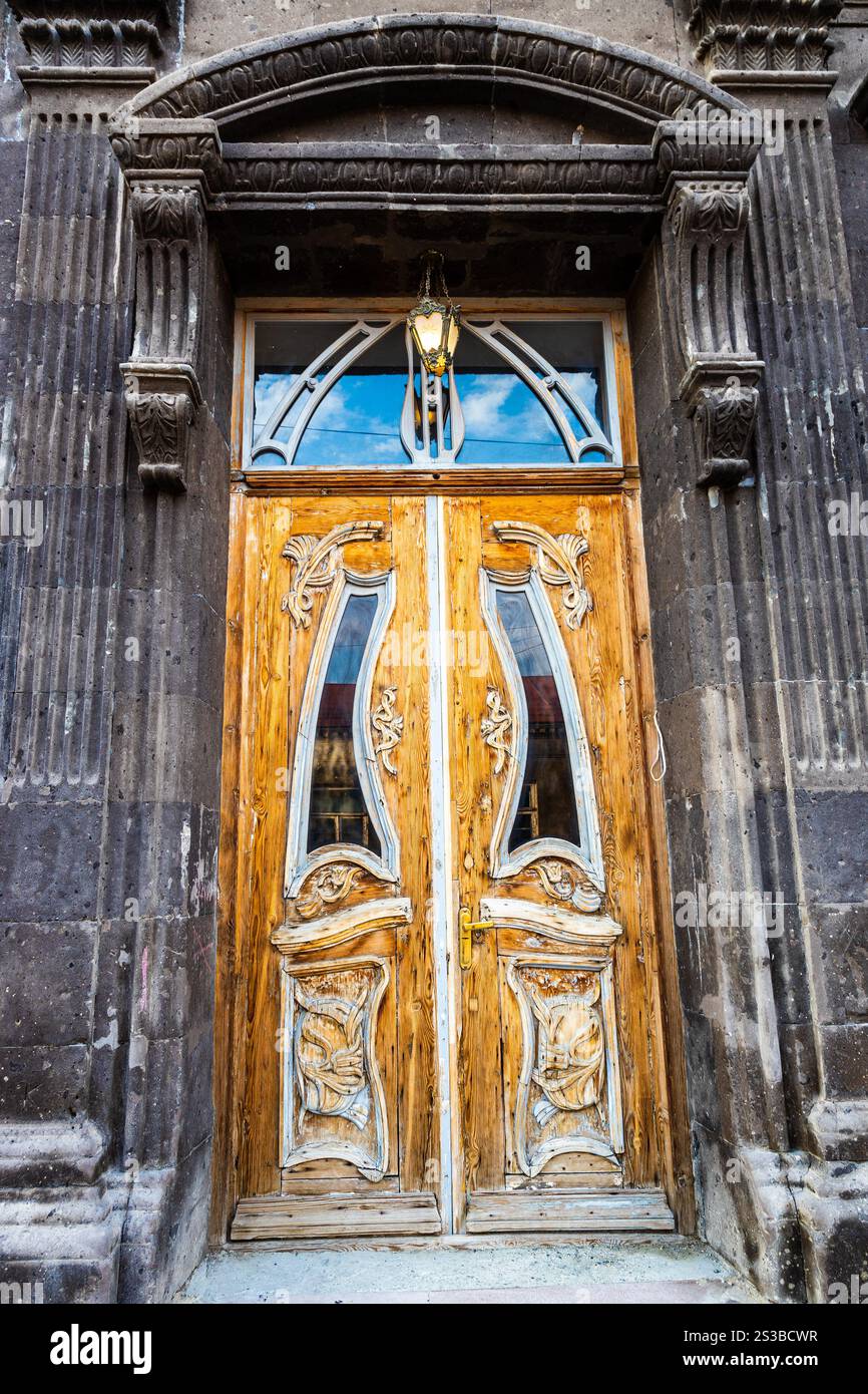 Porta in legno otnamentale di casa residenziale realizzata in tufo nero su Abovyan Street nella città vecchia di Gyumri, in Armenia al crepuscolo estivo Foto Stock