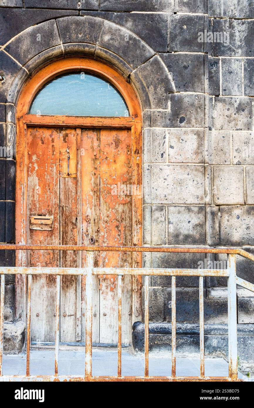 Porta in legno dipinta di arancio scura di casa residenziale realizzata in tufo nero su Abovyan Street nel centro storico di Gyumri, in Armenia al crepuscolo estivo Foto Stock