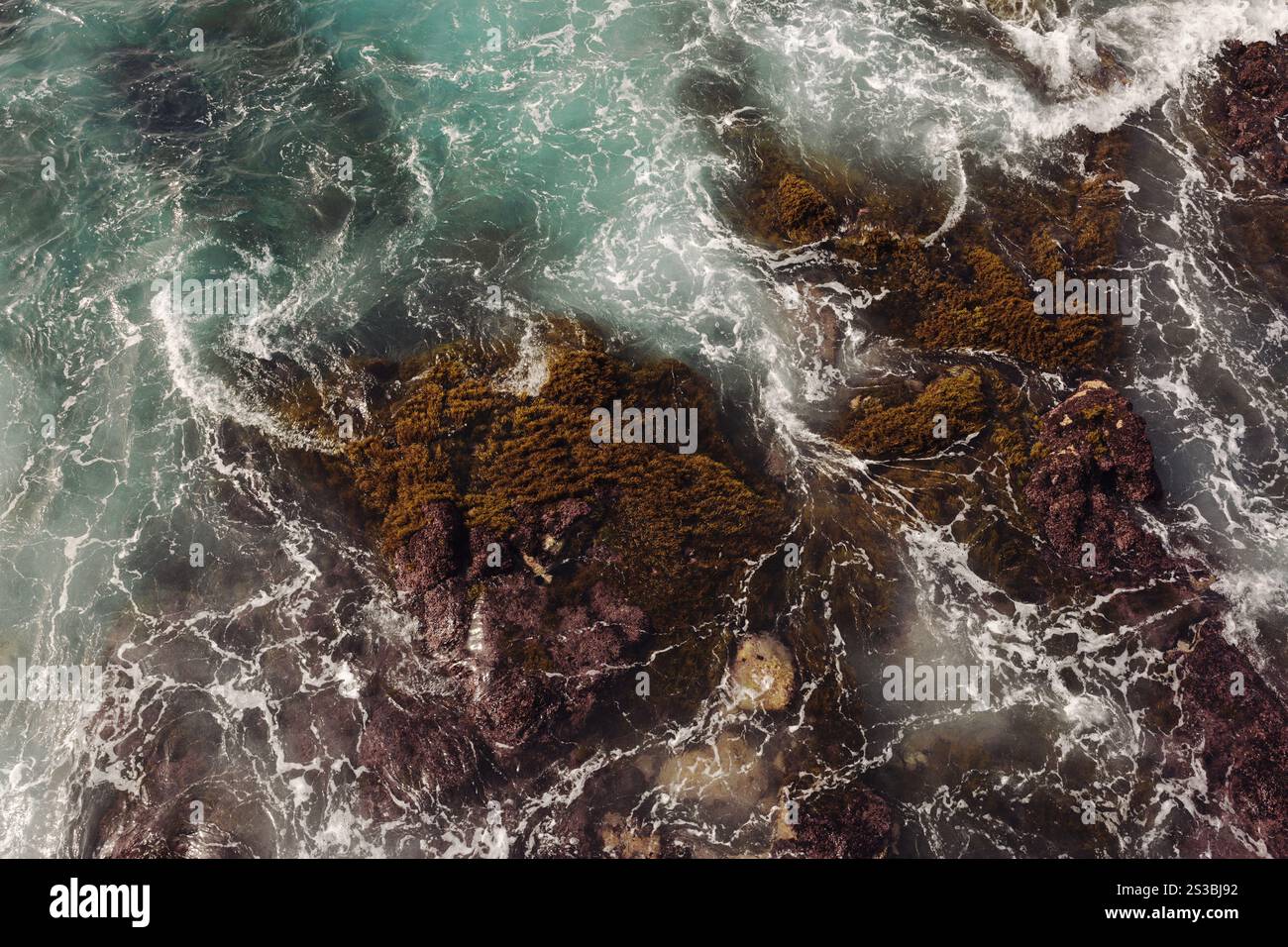 Onde marine con schiuma marina che si infrangono su rocce scure, vista dall'alto Foto Stock Onde marine con schiuma marina che si infrangono su rocce scure, vista dall'alto Foto Stock