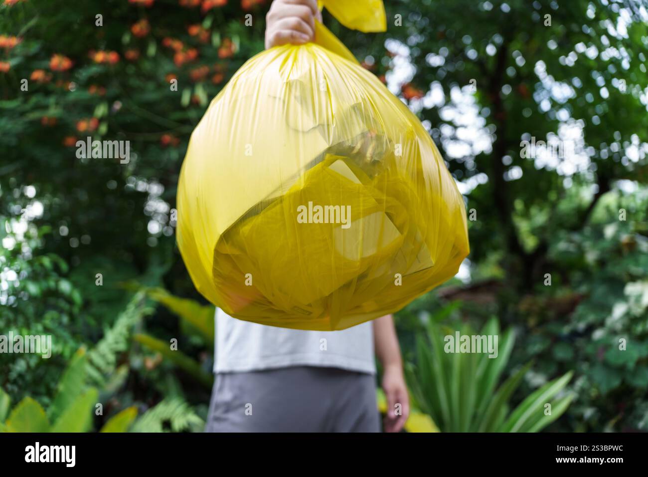 Man Volunteer Charity che tiene immondizia sacca gialla e bottiglia di plastica spazzatura per riciclare e pulire. Foto Stock