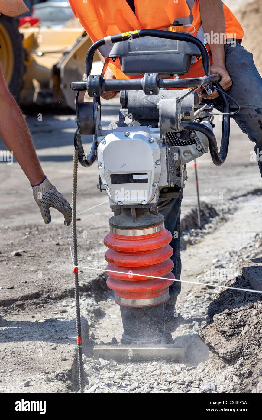 Operai edili che utilizzano un compattatore per preparare il terreno per il cantiere in condizioni di luce solare intensa Foto Stock