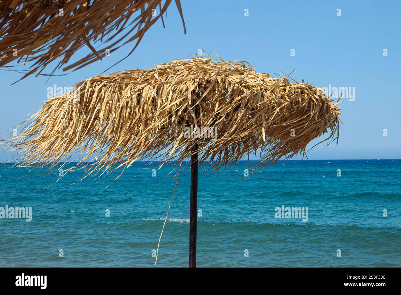 Materiale naturale ombrellone a foglie di canna asciutta contro le acque turchesi calme, cielo blu. Concetto di viaggio e vacanza. Foto Stock