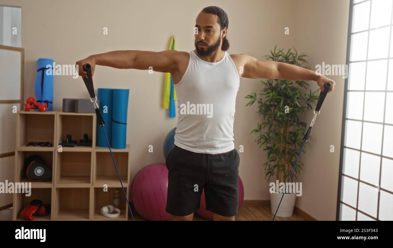 Giovane con barba che si esercita nel centro benessere con fasce di resistenza, mostrando fitness e forza in un ambiente interno sereno con attrezzature da palestra Foto Stock