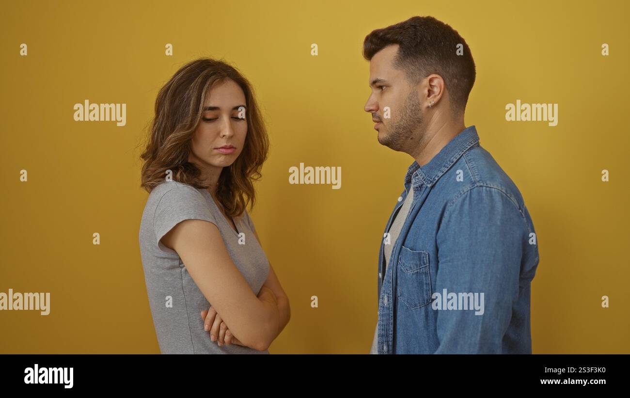 Uomo e donna in piedi su sfondo giallo, sembrano essere in una discussione o conflitto teso, isolati e seri Foto Stock