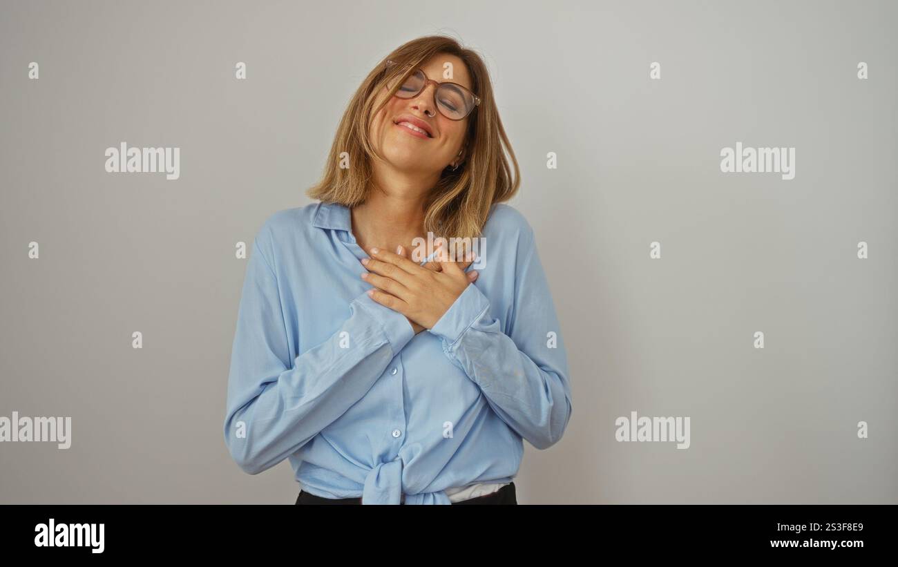 Giovane donna bionda sorridente con le mani sul cuore, isolata su uno sfondo bianco Foto Stock