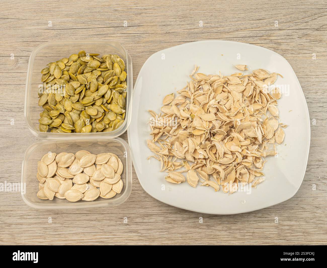 Semi di zucca pelati e bucce in contenitori su un tavolo di legno. Foto Stock