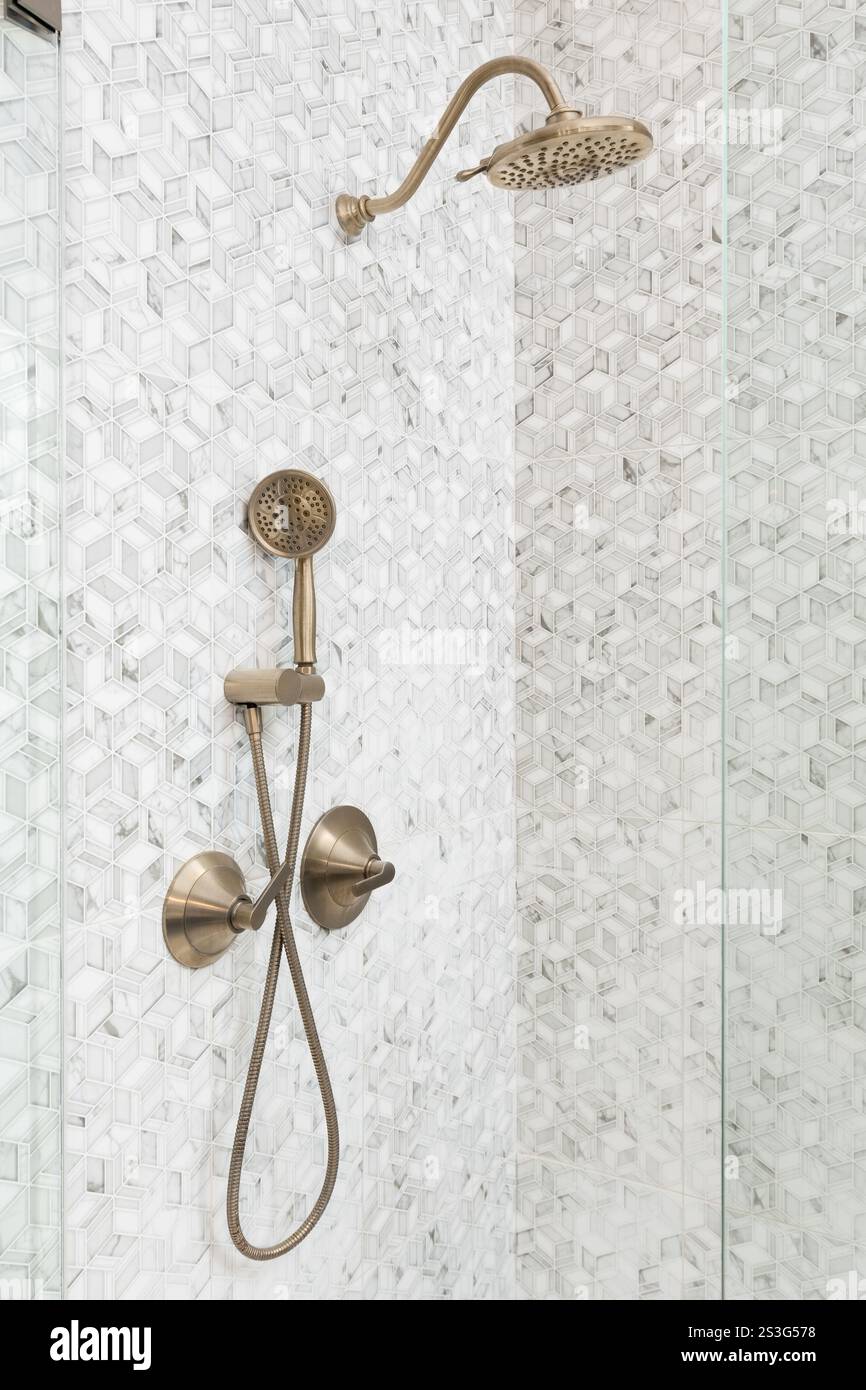 Una doccia con piastrelle a mosaico in marmo con motivo quadrato e soffione oro. Foto Stock