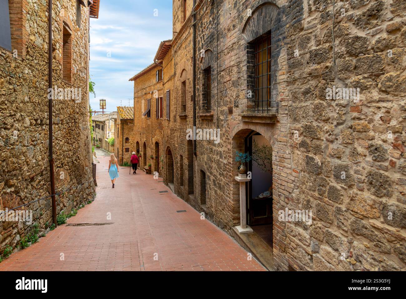 Una giovane donna cammina vicino a una donna anziana in uno stretto vicolo nel centro storico della collina di San Gimignano, in Italia, nella campagna toscana. Foto Stock