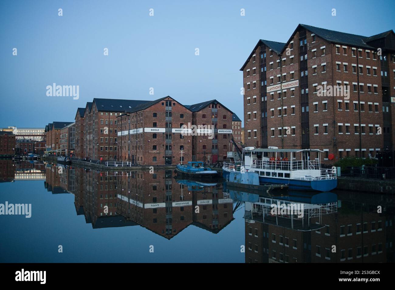 Un affascinante corso d'acqua con una fila di magazzini storici a Gloucester che costeggiano le sue rive. La scena invita all'esplorazione e al senso di scoperta. Foto Stock