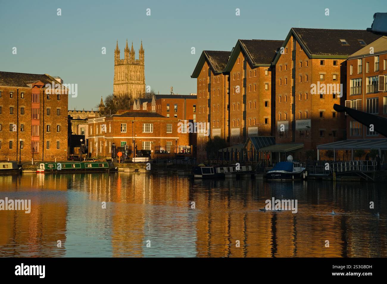 Un'affascinante scena urbana con lo storico Gloucester Quays e la maestosa Cattedrale di Gloucester. Il riflesso degli edifici nell'acqua Foto Stock