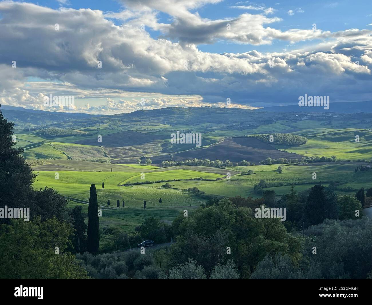 Splendida giornata primaverile a Pienza, Italia, con vista sulle lussureggianti colline toscane. I verdi vivaci, le nuvole spettacolari, il sole e la pioggia creano un'atmosfera da sogno, simile a quella di un dipinto - Immagine stock catturata con smartphone