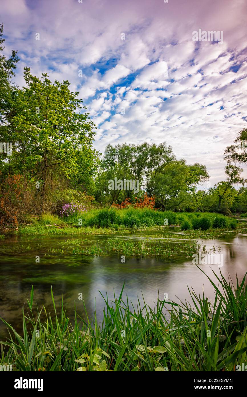 La corsa primaverile di Letort scorre attraverso un prato tranquillo e tranquillo con nuvole colorate rotte. Foto Stock