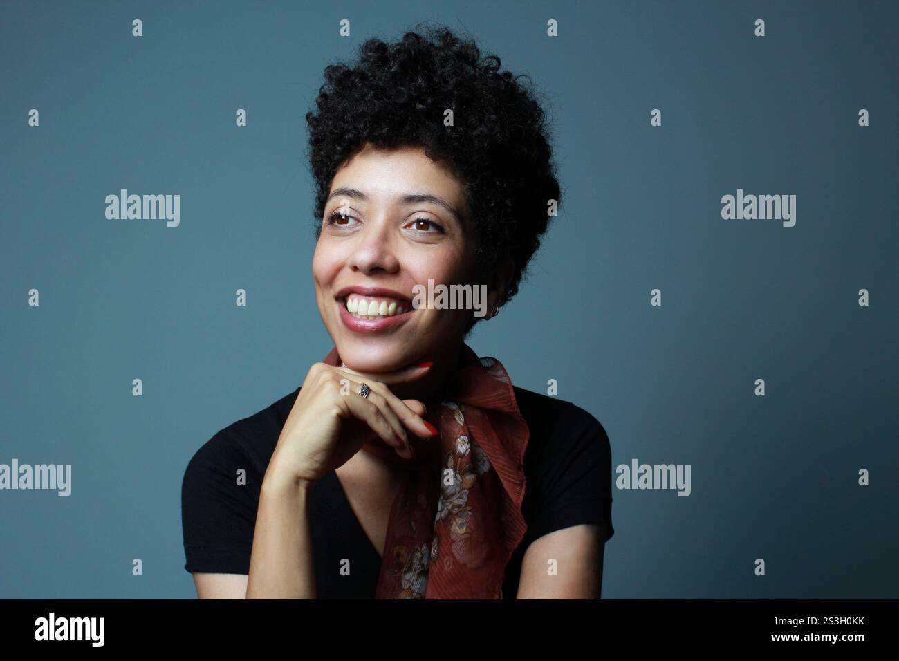 Donna dalla pelle marrone che sorride e guarda lateralmente. Abito da modella femminile con capelli ricci corti, elegante e casual. Striscione orizzontale con spazio di copia. Foto Stock
