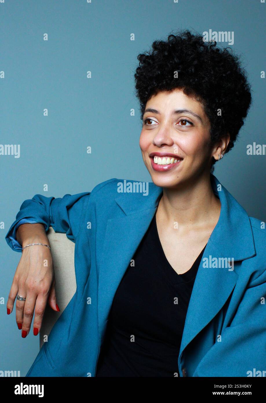 Donna d'affari di successo seduta rilassata su una sedia. La modella afro americana con capelli ricci corti indossa un abbigliamento da ufficio. Foto Stock