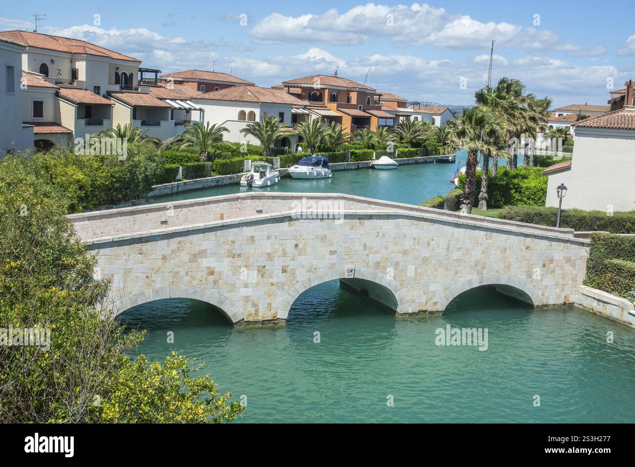 Ponte sul canale con barche per il tempo libero al molo e con palme e case vacanza a Lido di Policoro, Basilicata, Mar Mediterraneo, Italia, S. Foto Stock