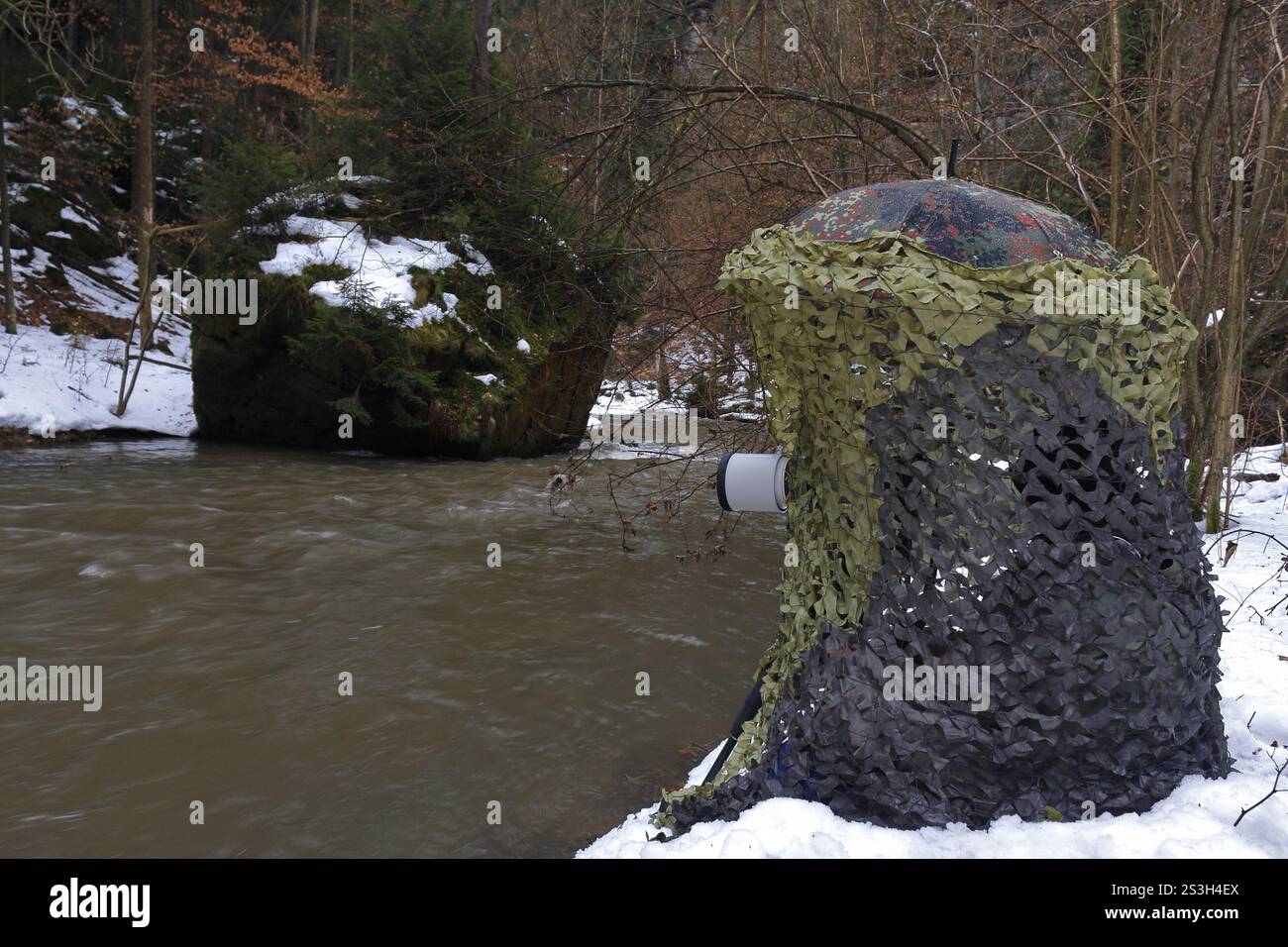 Fotografo naturalistico in un nascondiglio mimetico sulle rive di un torrente di montagna in inverno, Svizzera sassone, Elba Sandstone Mountains, Sassonia, tedesco Foto Stock