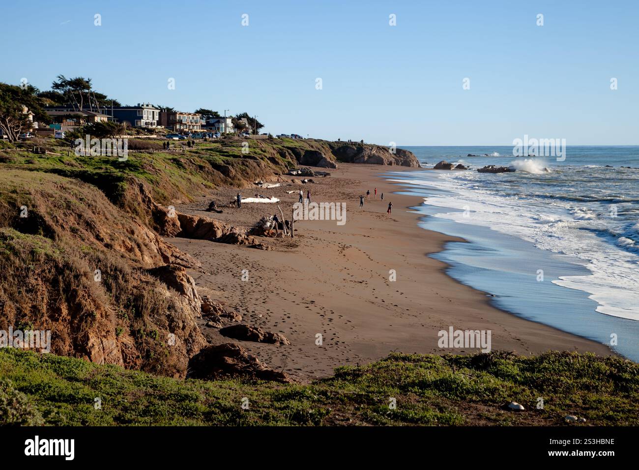 Moonstone Beach presenta dolci onde che si infrangono sulla riva mentre la gente passeggiava lungo la costa sabbiosa. Le scogliere sorgono dietro con case visibili nel di Foto Stock