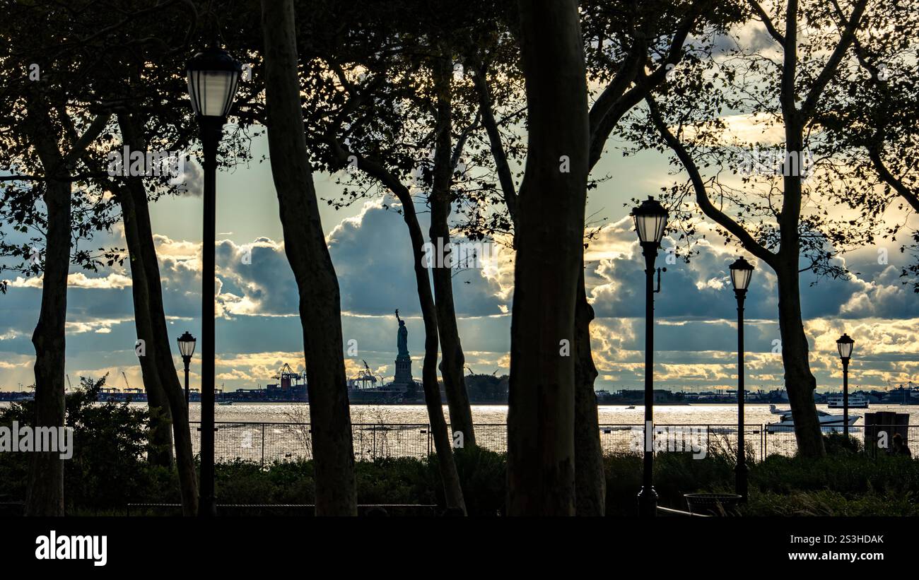 Silhouette serena della Statua della libertà incorniciata da alberi e lampioni nel pomeriggio, che unisce natura, architettura e storia iconica in un'unica vista Foto Stock Silhouette serena della Statua della libertà incorniciata da alberi e lampioni nel pomeriggio, che unisce natura, architettura e storia iconica in un'unica vista Foto Stock