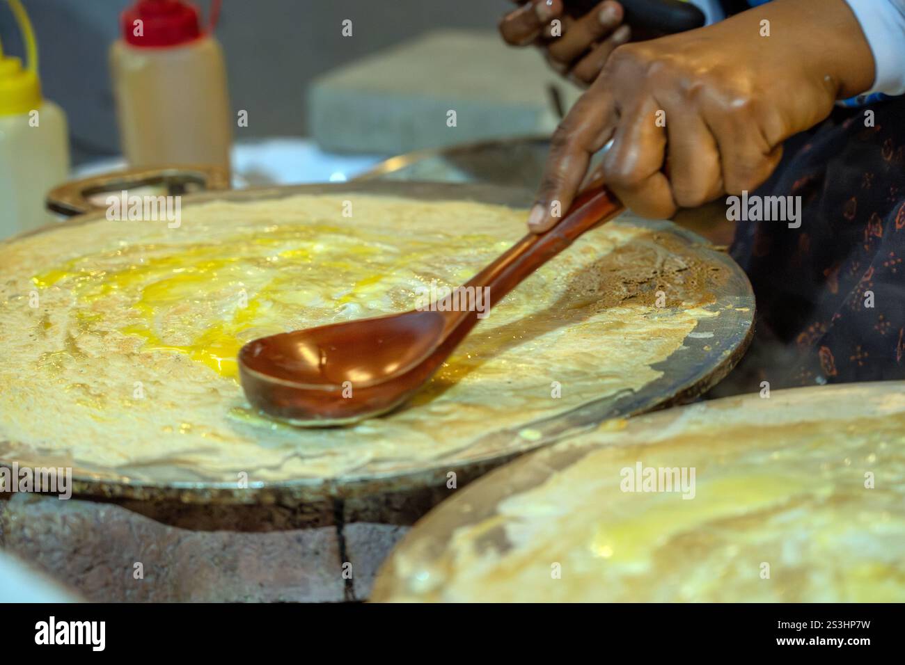 Uno chef distribuisce sapientemente il burro sul pane omanita, noto come Kuboos, su una grigliata calda. Questa prelibatezza tradizionale è un punto fermo della cucina omanita, fatta con l'ingegno Foto Stock