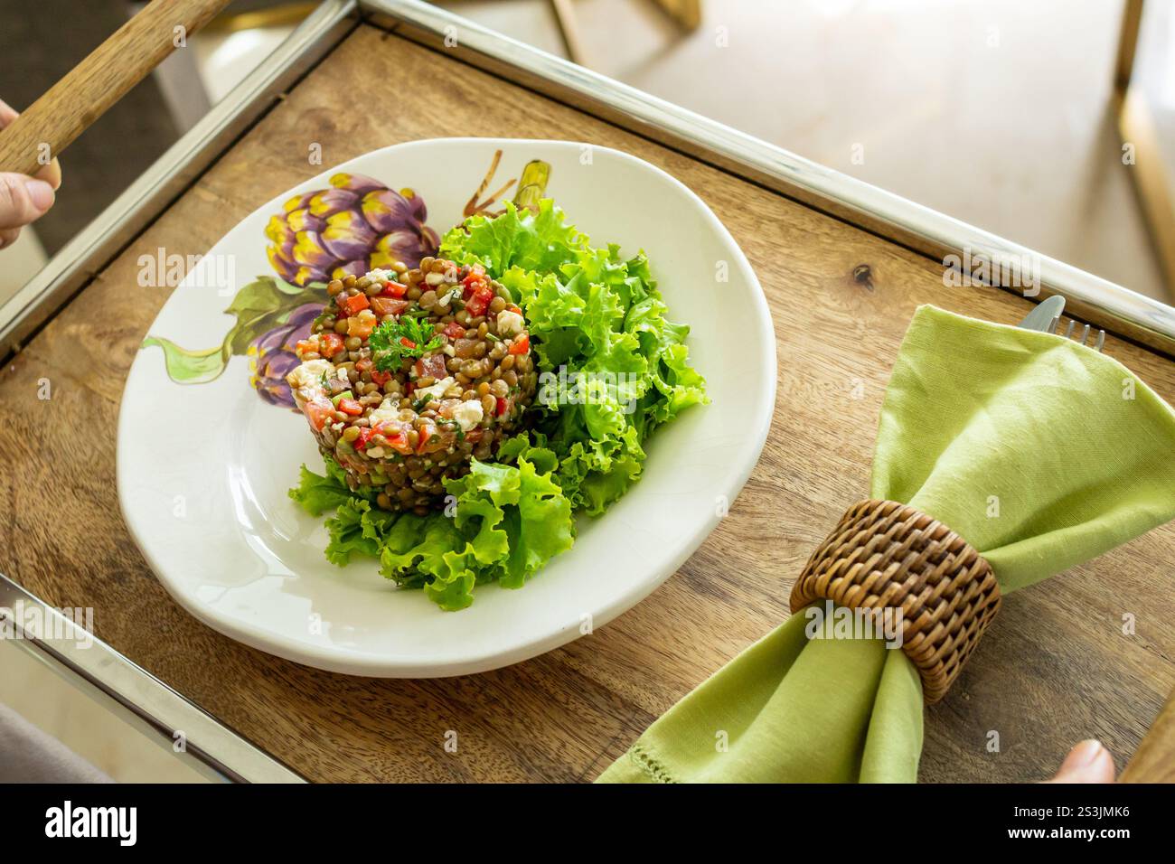 Vista ravvicinata ragazza che tiene un vassoio di insalata di lenticchie e formaggio fresco decorato a lato con la sua tovaglia, pasto sano Foto Stock