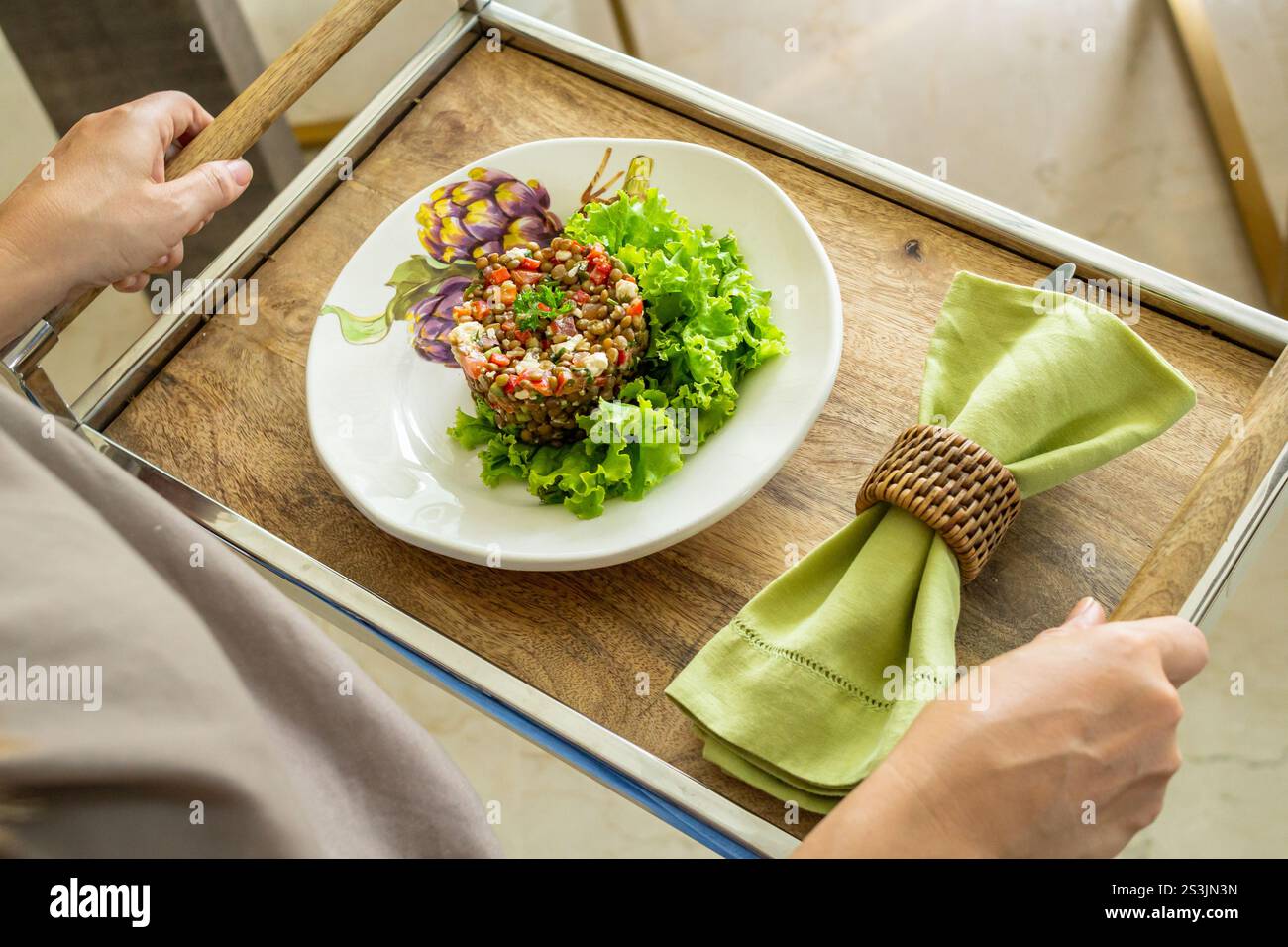 Vista ravvicinata ragazza che tiene un vassoio di insalata di lenticchie e formaggio fresco decorato a lato con la sua tovaglia, pasto sano Foto Stock