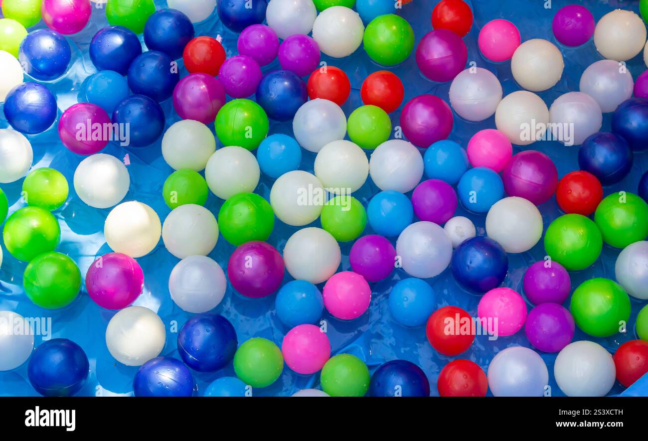 Palline dai colori vivaci nelle sfumature di blu, verde, rosa, bianco e rosso galleggiano sulla superficie di una piscina limpida, riflettendo la luce del sole e creando Foto Stock