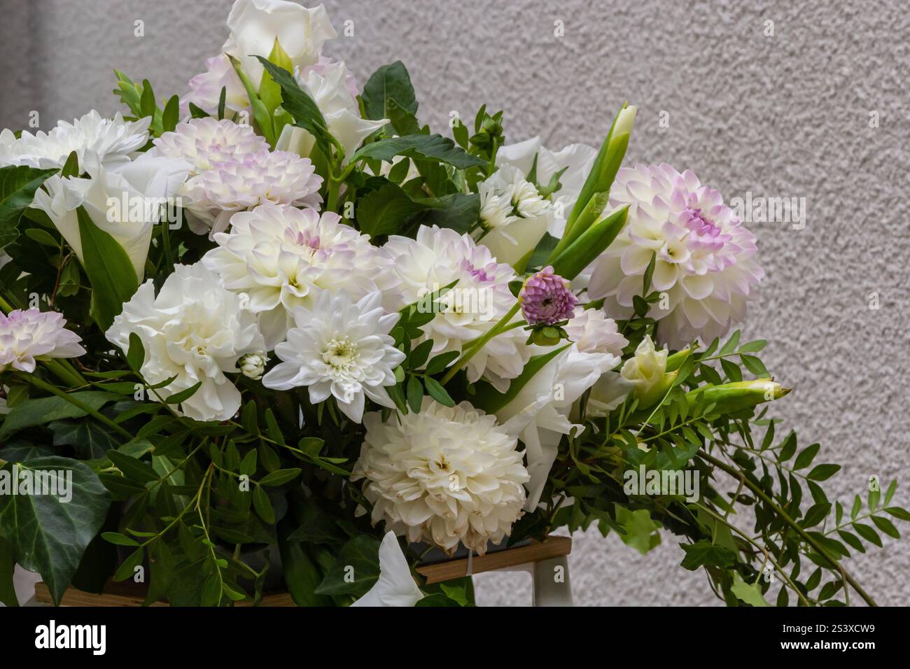 Un bouquet splendidamente organizzato di fiori bianchi, tra cui dahlia e gigli, si trova su una parete grigia testurizzata, creando un'atmosfera tranquilla Foto Stock
