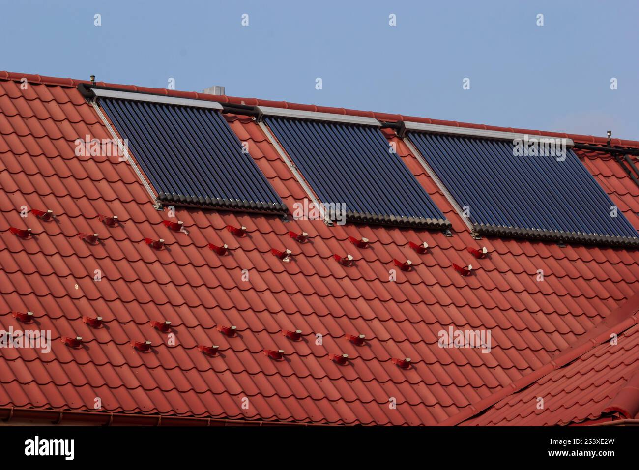 I pannelli solari installati su un tetto piastrellato di colore rosso riflettono la luce del sole mentre generano energia rinnovabile. Questa impostazione promuove la sostenibilità e l'efficienza energetica Foto Stock