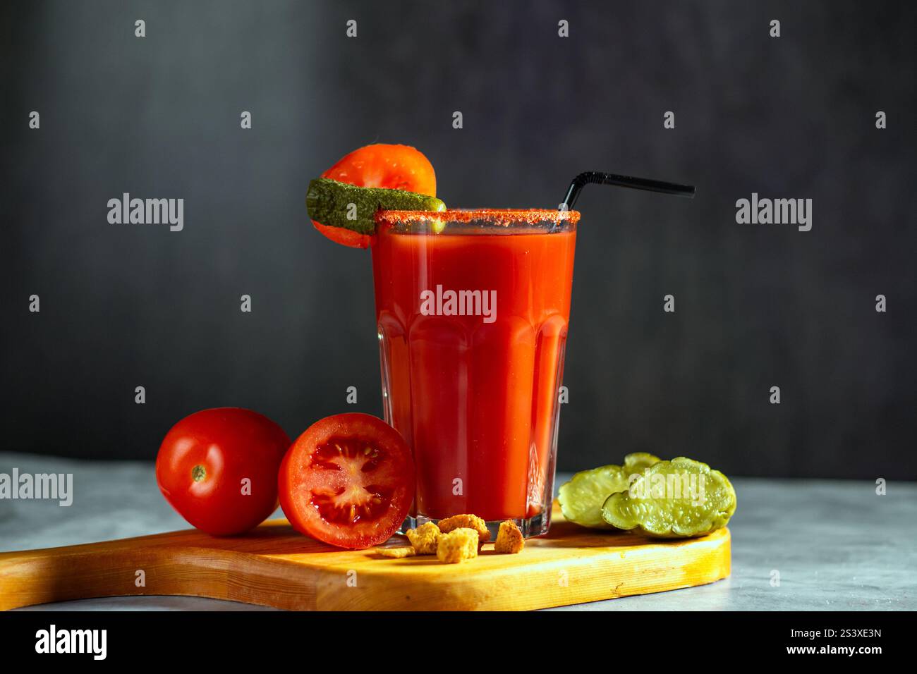 Cocktail agitato di verdure in vetro su sfondo grigio scuro. Cocktail di pomodoro rosso. Servito con pomodori e sottaceti. Menu vegano. Foto Stock
