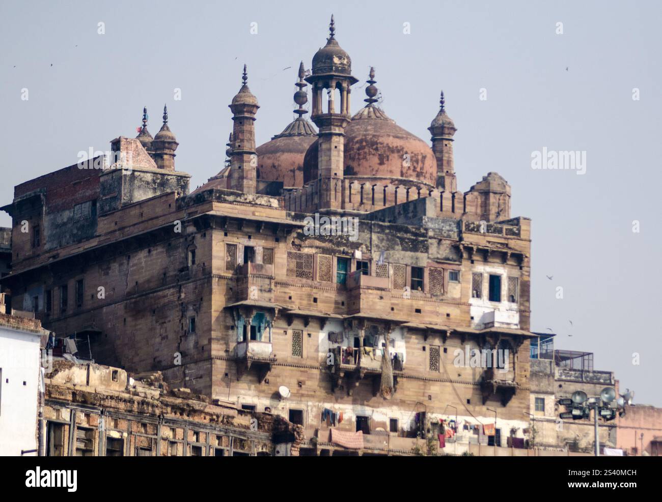 Vista dell'architettura storica lungo la riva del fiume con barche colorate a Varanasi durante il giorno Foto Stock