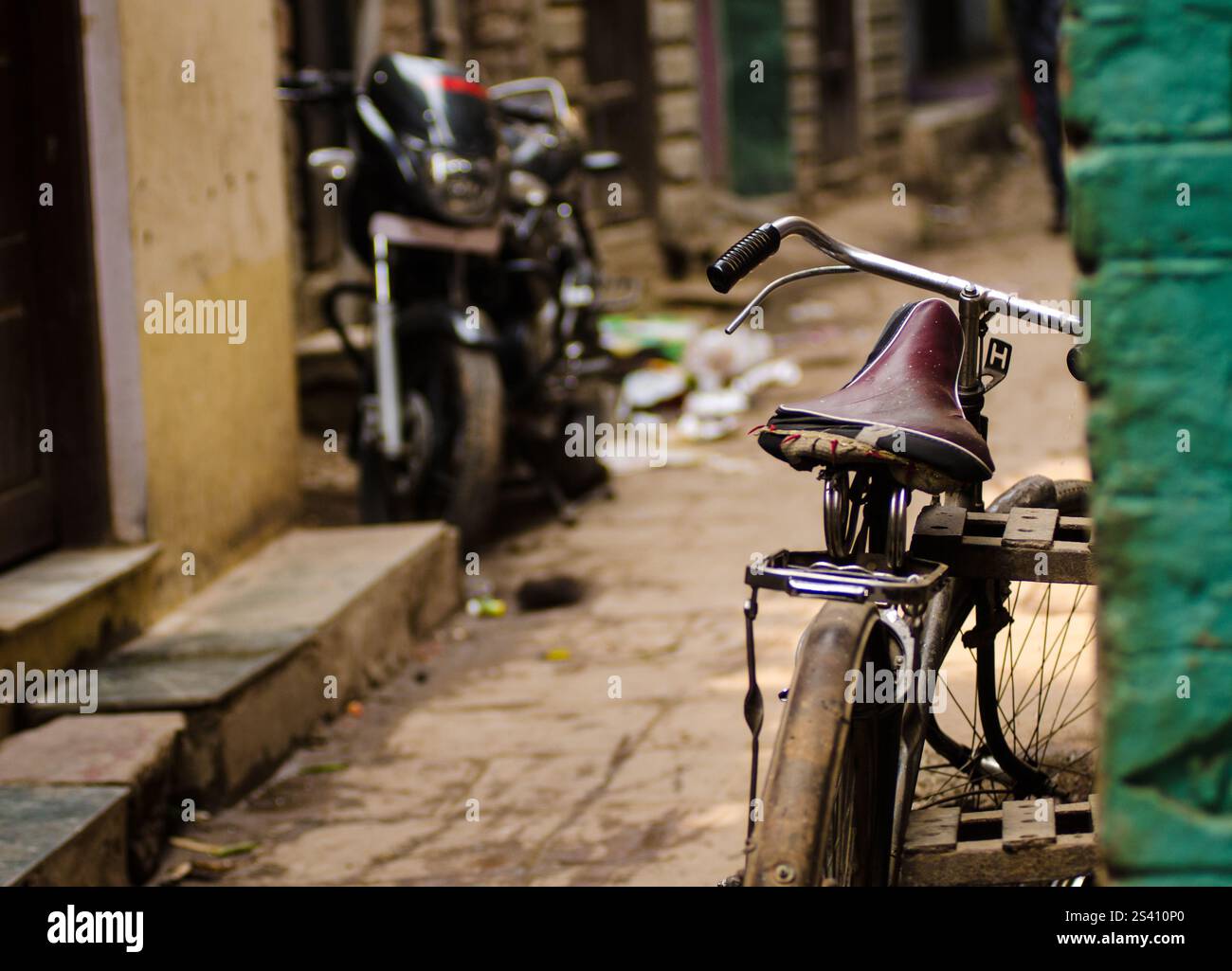 Una bicicletta d'epoca si appoggia su un muro colorato in uno stretto vicolo durante il giorno. Una motocicletta è parcheggiata nelle vicinanze, circondata da detriti sparsi. Foto Stock