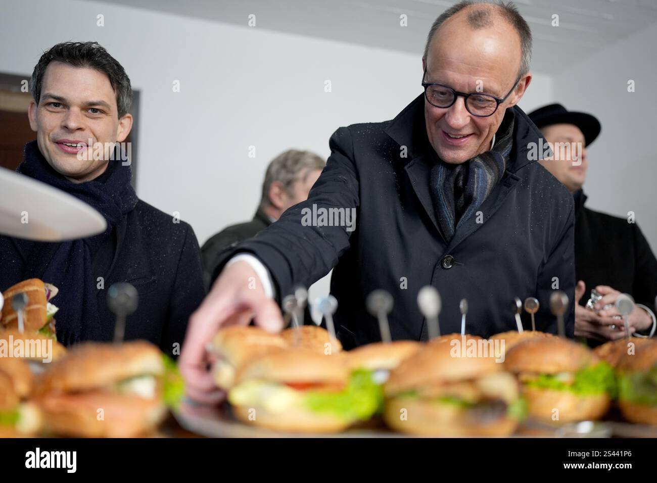 Amburgo, Germania. 10 gennaio 2025. Friedrich Merz (r), candidato alla carica di cancelliere e presidente del partito CDU, afferra un panino di pesce durante una visita alla VB-Industries GmbH nel porto. A sinistra si trova Christoph Ploß (CDU), presidente del gruppo regionale di Amburgo del Bundestag tedesco. VB-Industries è specializzata nei settori dell'ingegneria di processo degli impianti per la generazione di energia, nonché nelle tecnologie per cantieri navali e di gestione navale. Credito: Marcus Brandt/dpa Pool/dpa/Alamy Live News Foto Stock