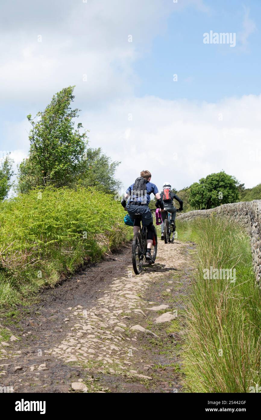 Due ciclisti su una pista sterrata che conduce attraverso il paesaggio brughiero della riserva naturale di Blacka Moor, Peak District, Regno Unito Foto Stock