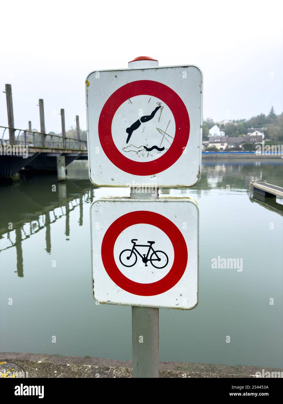 Non ci sono segni di nuoto e di ciclismo vicino al tranquillo corso d'acqua vicino al molo in una posizione tranquilla in una giornata nuvolosa Foto Stock