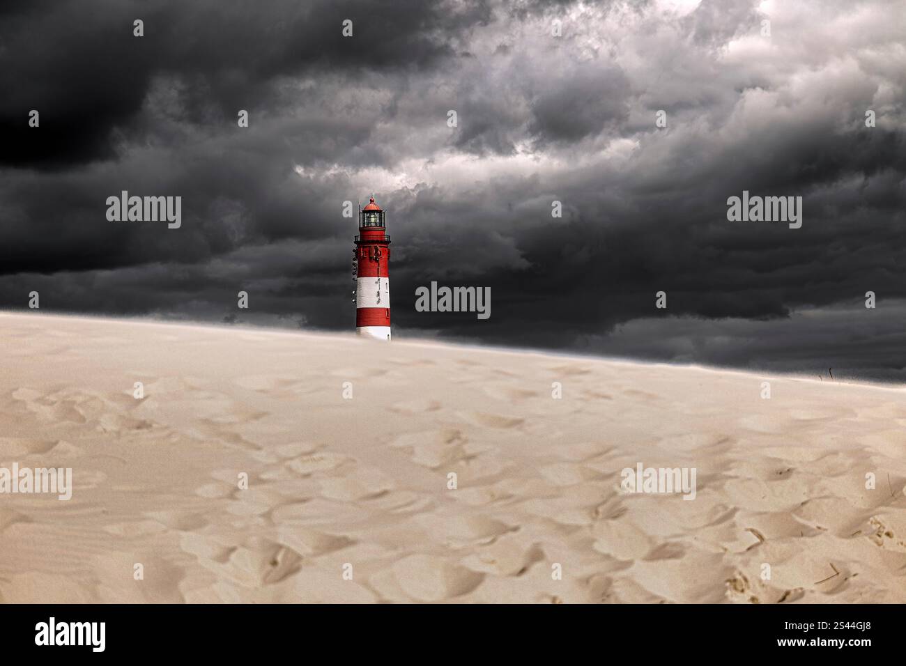 Un faro solitario sorge su una duna di sabbia sotto un cielo minaccioso, grigio e nuvoloso Foto Stock