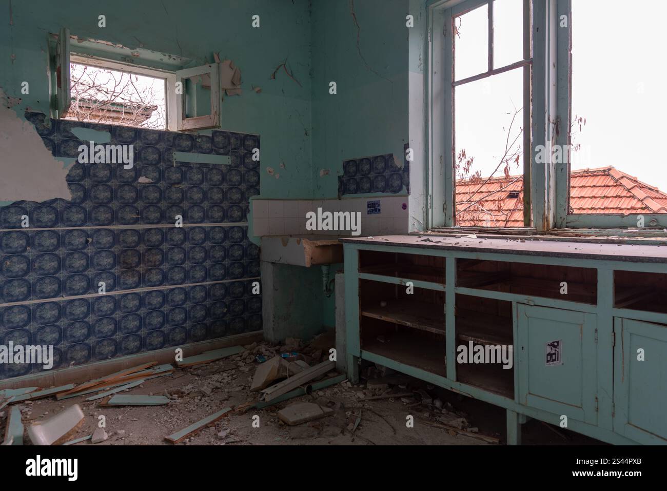 Cucina in decadenza con finestra rotta e vernice sbucciata in casa abbandonata, che illustra il degrado urbano Foto Stock