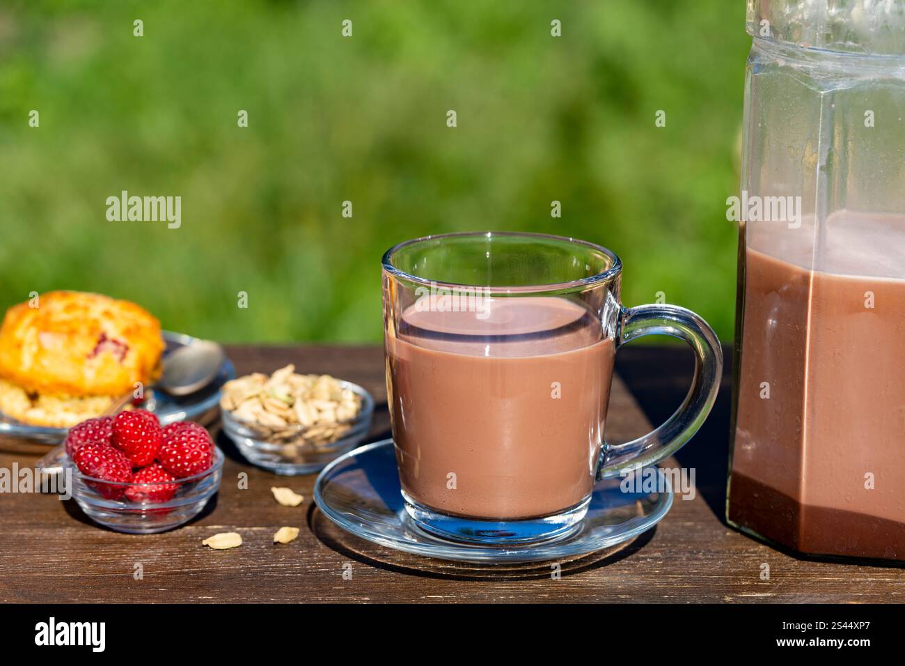 Masala chai indiano o tè o cacao in vetro con brocca e muffin ai lamponi sul tavolo di legno nel caffè sullo sfondo naturale, primo piano. Trendy salutare d Foto Stock
