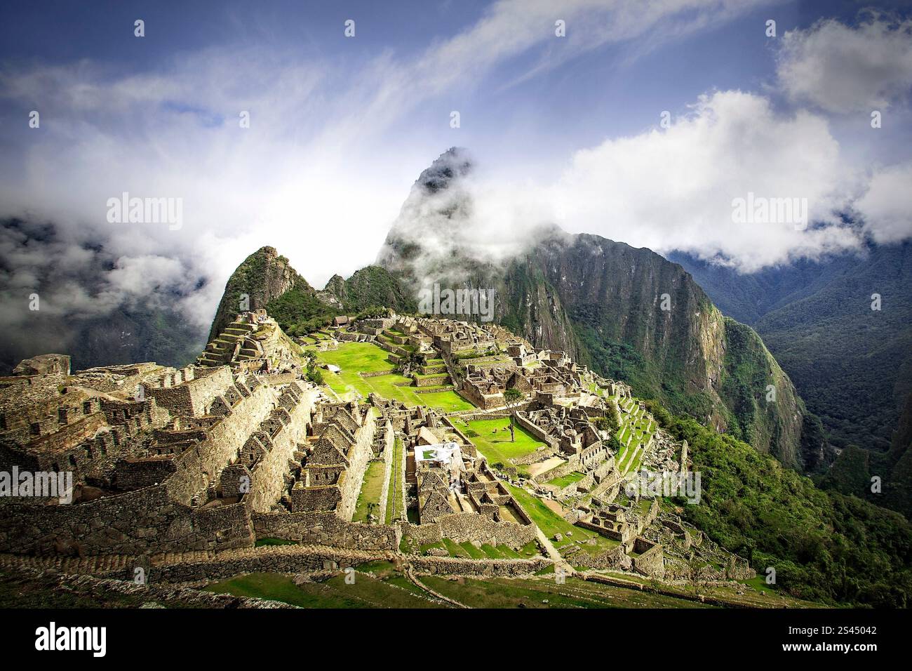 Mentre il sole mattutino sorge su Machu Picchu, dissolve la nebbia persistente che avvolge Huayna Picchu, rivelando la sua maestosa presenza. Foto Stock