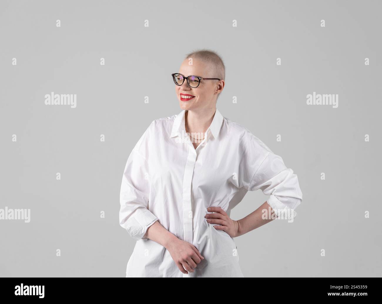 Ritratto di una bella giovane donna caucasica con la testa rasata. Sopravvissuta al cancro femminile. Sorridere con gli occhiali in posa in modo sicuro in uno Studio. Un portrai Foto Stock