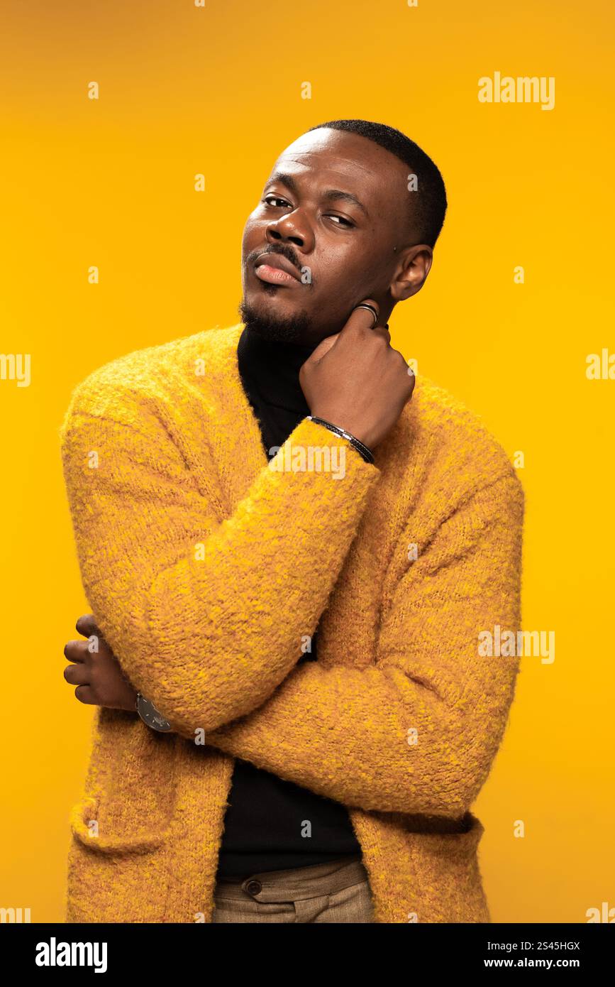 Un uomo con un elegante cardigan giallo posa con sicurezza su uno sfondo vibrante, incarnando un senso di moda e individualità. Foto Stock
