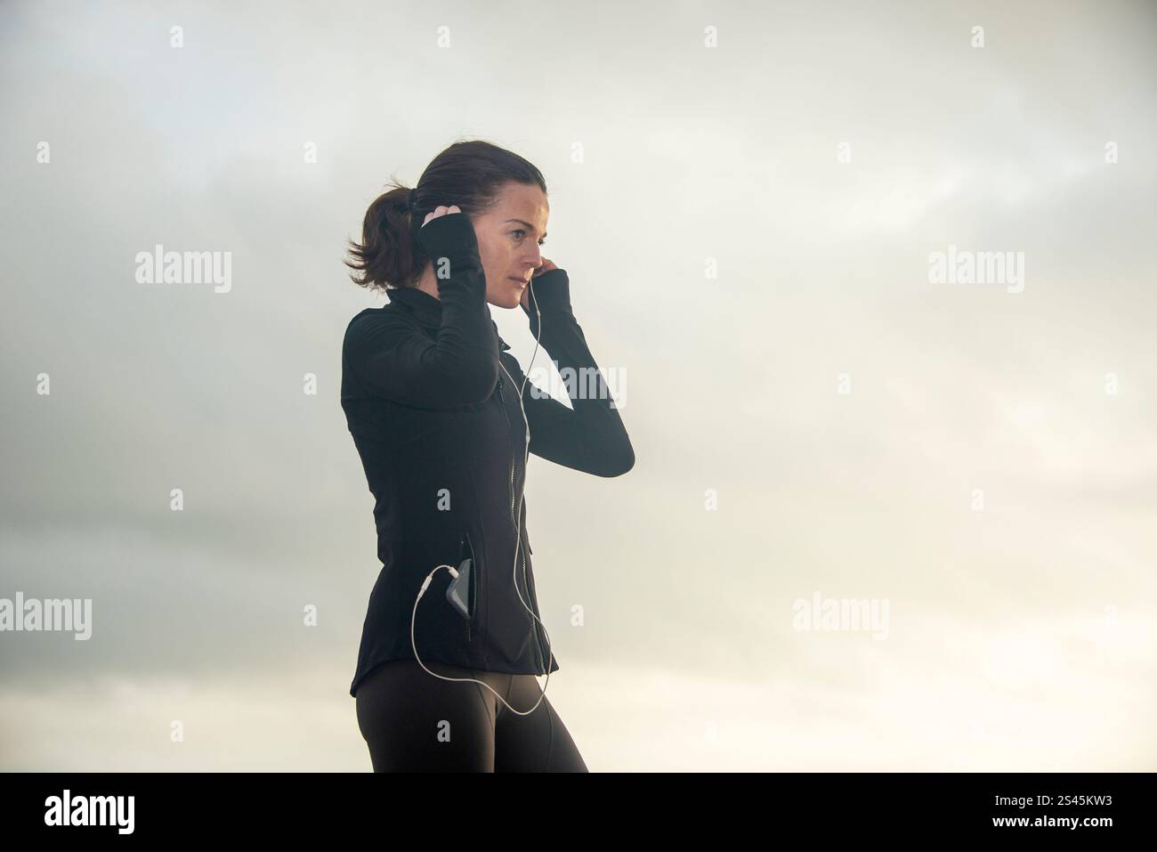 jogger donna che regola le cuffie, all'aperto Foto Stock