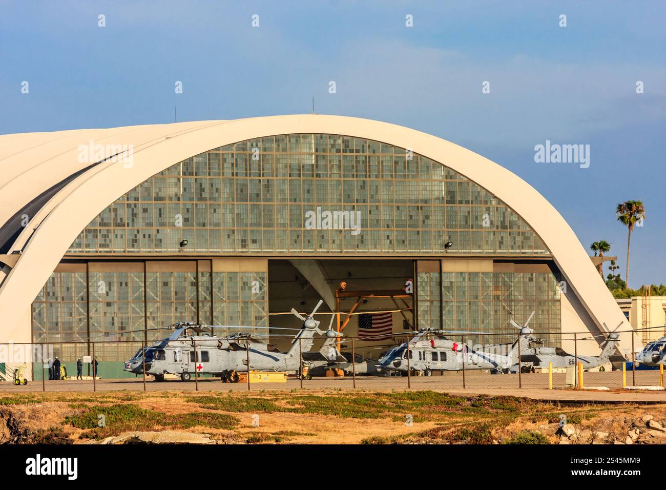 Un hangar con un grande arco e diversi elicotteri parcheggiati all'interno. L'hangar è bianco e gli elicotteri sono rossi e bianchi Foto Stock