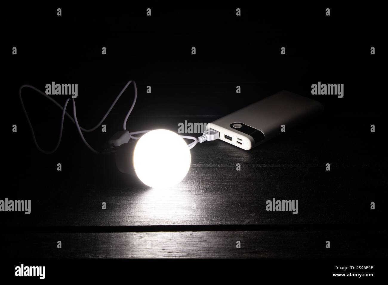 Una lampadina a risparmio energetico collegata a una batteria esterna si trova sul tavolo, Ucraina senza luce Foto Stock