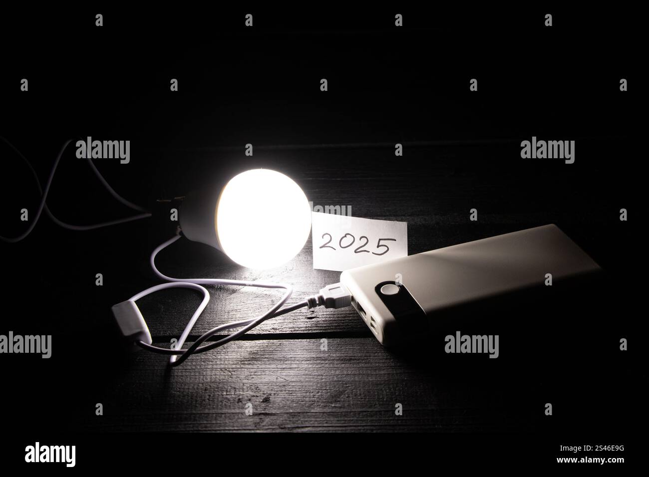 Una lampadina a risparmio energetico collegata a una batteria esterna e una scheda con l'anno 2025 scritto su di essa si trova sul tavolo, Ucraina senza elettricit Foto Stock