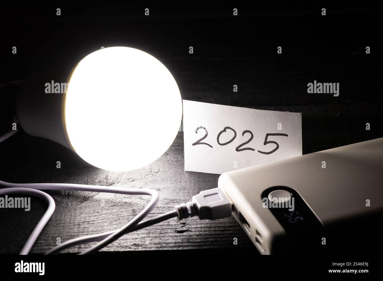 Una lampadina a risparmio energetico collegata a una batteria esterna e una scheda con l'anno 2025 scritto su di essa si trova sul tavolo, Ucraina senza elettricit Foto Stock