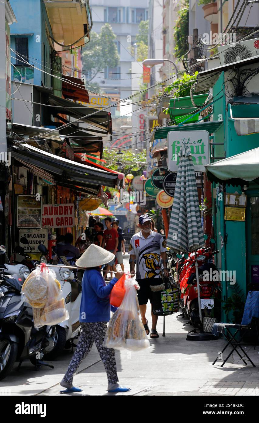 Ho chi Minh City, Vietnam - 9 dicembre 2022: Il venditore di strada indossa il tradizionale cappello conico, non la, mentre lavora nell'area turistica del Distretto 1. Foto Stock