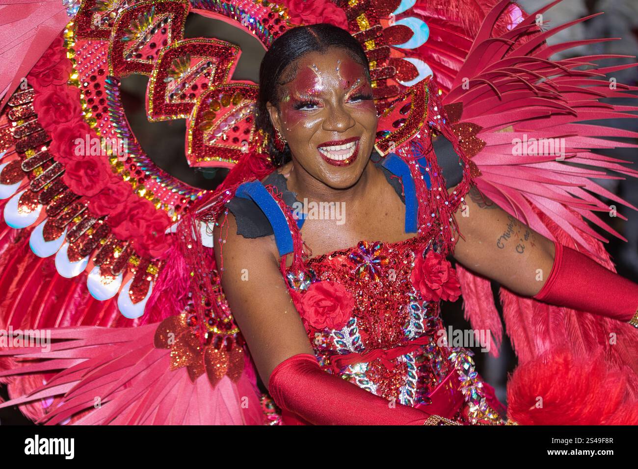 Una giovane donna nera vestita con un costume rosso brillante con piume bianche, vernice per il viso e un capo colorato ballato per strada durante il giorno di Santo Stefano Foto Stock