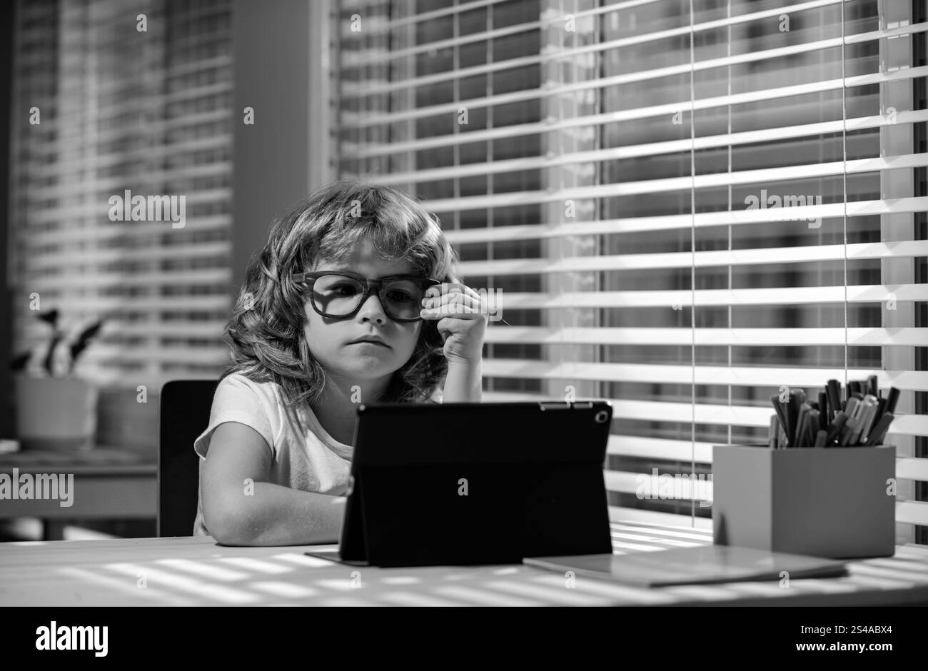 Bambino scolaro in occhiali, allievo intelligente con tablet a casa, apprendimento online in remoto, homeschooling, social distancing con facetime zoom, google Foto Stock