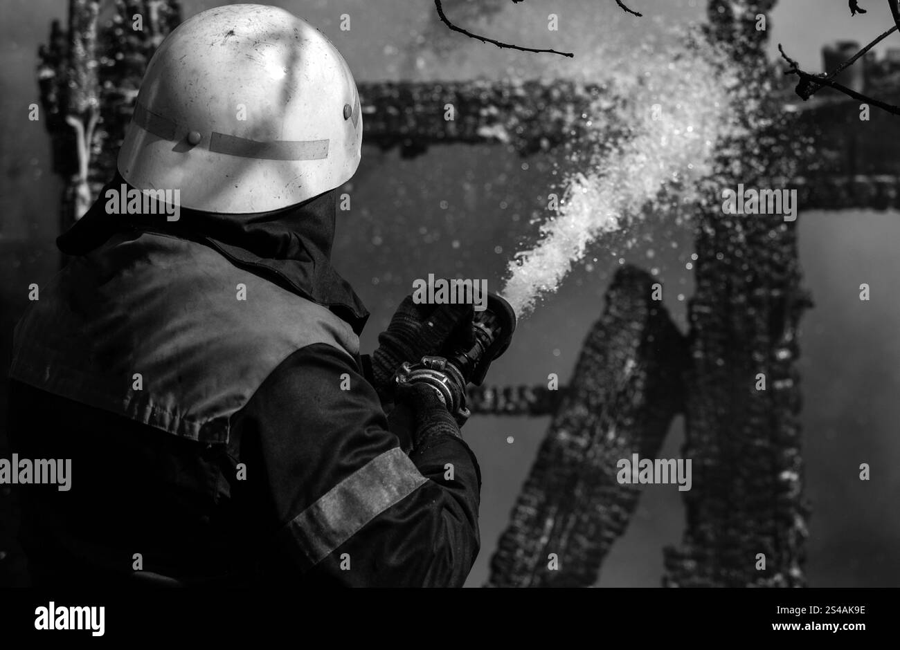 Coraggioso vigile del fuoco che salva l'edificio in fiamme. Concetto di lavoro dei pompieri. I vigili del fuoco utilizzano l'acqua nelle operazioni antincendio. Combattimenti da eroe davvero coraggiosi Foto Stock